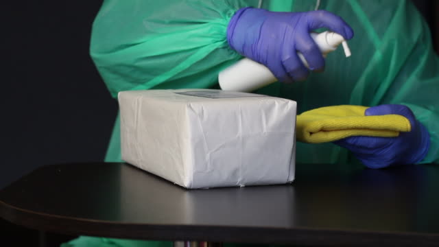 Delivery of correspondence during a pandemic. A man in rubber gloves and a raincoat processes the received parcel with an antiseptic and wipes it with a napkin. Symbol of the fight against the pandemic.