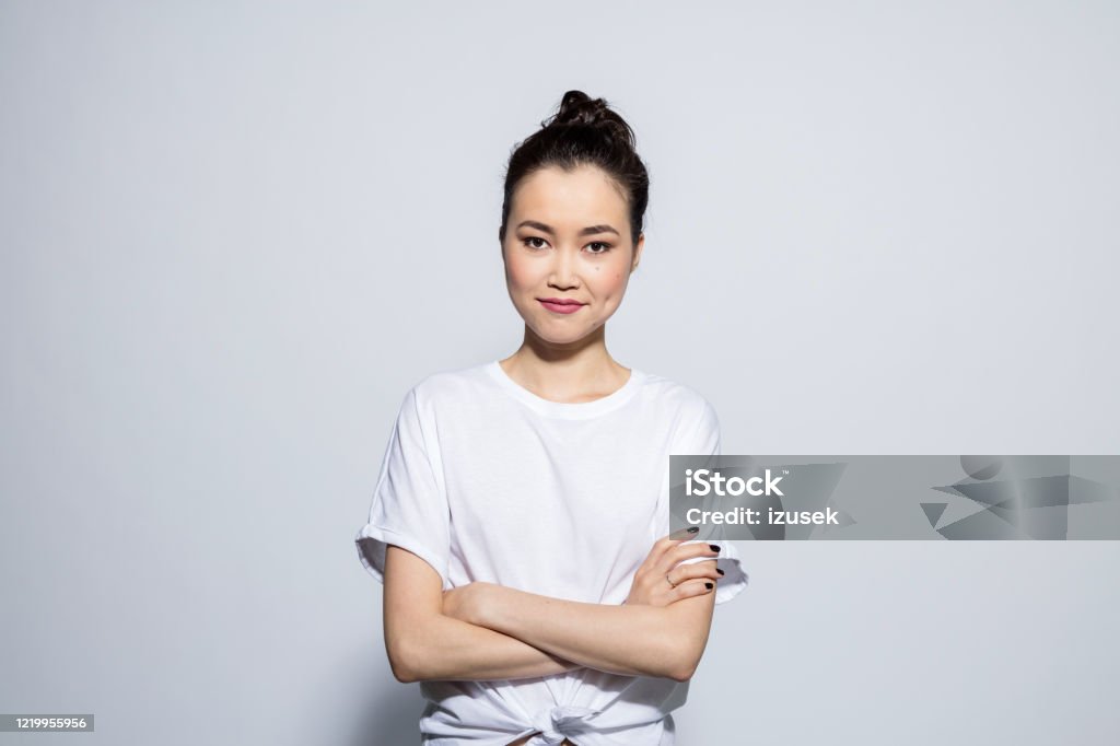 Smiling beautiful asian young woman Portrait of beautiful asian young woman wearing white t-shirt, smiling at camera. Studio shot, grey background. Portrait Stock Photo