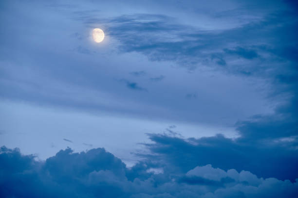 The moon hiding behind some clouds on an dramatic evening sky in summer in Germany in August.