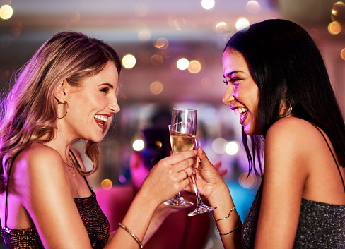 Cropped shot of two cheerful young women having a celebratory toast with drinks inside of a bar at night