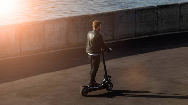 istock Modern man with technological electric kick scooter. Concept with copy space at the street in good weather. He is driving personal e-scooter alone in a city 1219957251