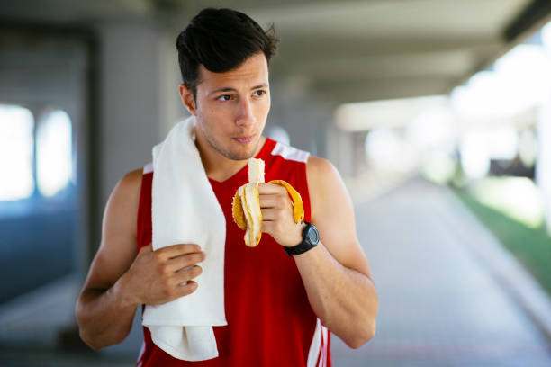 屋外でトレーニング後にバナナを食べるアスレチックマン - sport food exercising eating ストックフォトと画像
