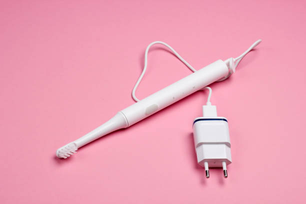 istock Modern electric toothbrush with a charger on a pink pastel background. 1219963490
