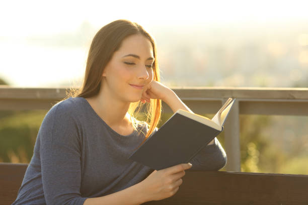 istock Woman reading a hard cover book at sunset on a park 1219963790