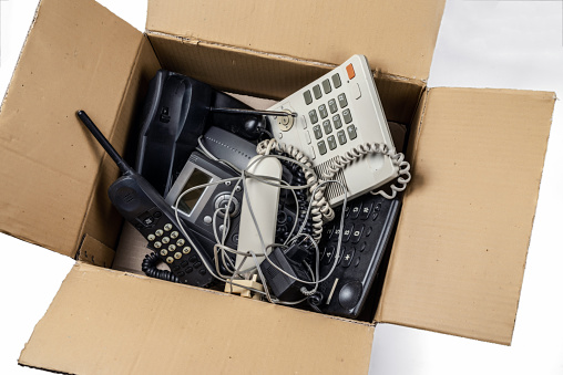 Old desk phones in a cardboard box. On a white background.