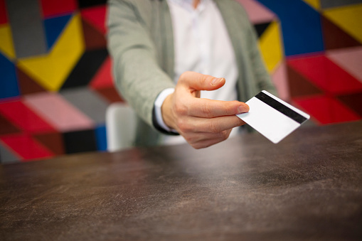 Close up of hand giving credit card above table.