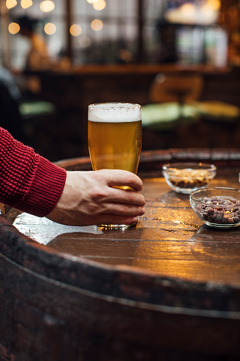 An unrecognizable man's hand holding a glass of craft beer at a bar.