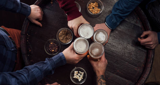Hands of People Toasting with Beer at a Pub Unrecognizable men celebrating by  toasting with glasses of beer at a local bar. craft beer photos stock pictures, royalty-free photos & images