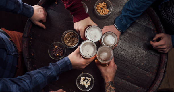 Hands of People Toasting with Beer at a Pub Unrecognizable men celebrating by toasting with glasses of beer at a local bar. pub table top view stock pictures, royalty-free photos & images