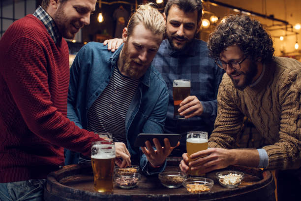 group of friends watching football on a smartphone and drinking beer at a pub together - club soccer imagens e fotografias de stock