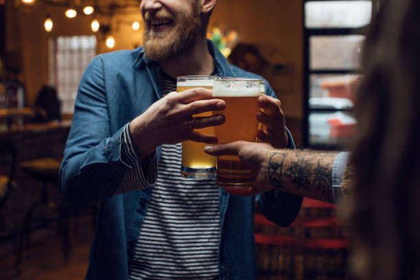 Happy Blond Hipster Man Bringing Beer for his Friends at a Pub, a Close Up Happy hour at the bar: smiling man bringing beer for his mates. craft beer stock pictures, royalty-free photos & images