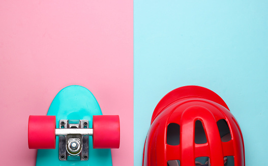 Cruiser board and safety helmet on pink blue pastel background. Protective equipment for sports. Childhood. Top view