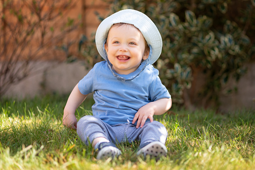 Baby boy 10 months old looking away and smiling whilst sitting in the shade in the garden on a sunny day