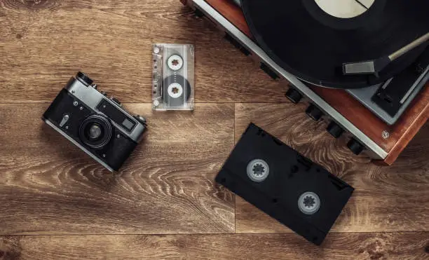 Old vinyl record player, video cassettes, audio cassette, old-fashioned film camera on the floor. Retro media 80s. Top view