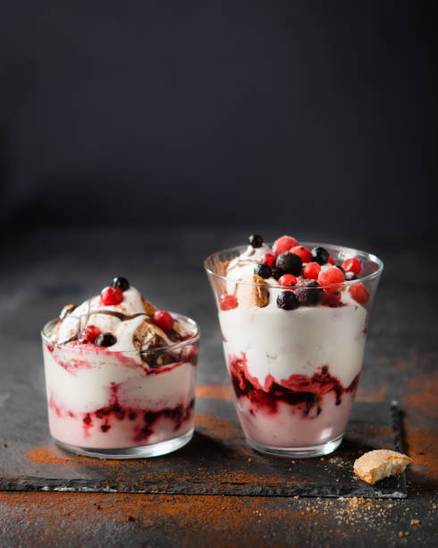 sciocchezza di frutta rossa, tiramisù, parfait stratificato con panna montata, sciroppo di cioccolato e dita o biscotti da signora su sfondo scuro. messa a fuoco selettiva. niente dessert estivo al forno. - tiramisu trifle italian culture dessert foto e immagini stock