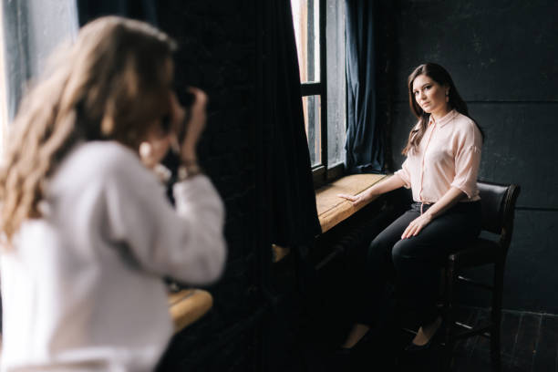 istock Woman model posing while sitting on chair in photo studio for unrecognizable female photographer 1219973574