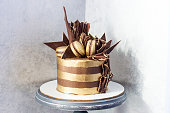 Chocolate birthday cake with golden stripes, dark chocolate decoration and macaroons.