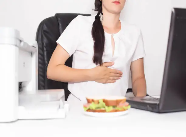 Photo of Girl office worker near which lies a sandwich holding on to a stomach in which there is pain and inflammation in the stomach. Concept of indigestion and malnutrition in office workers, gastritis and duodenal ulcer