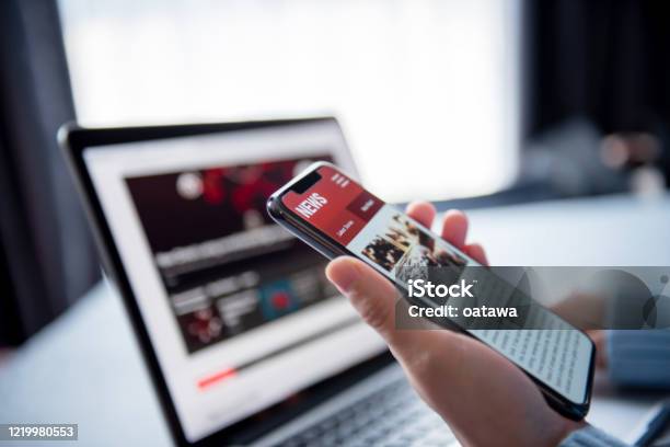 Online News On A Smartphone And Laptop Woman Reading News Or Articles In A Mobile Phone Screen Application At Home Newspaper And Portal On Internet Stock Photo - Download Image Now
