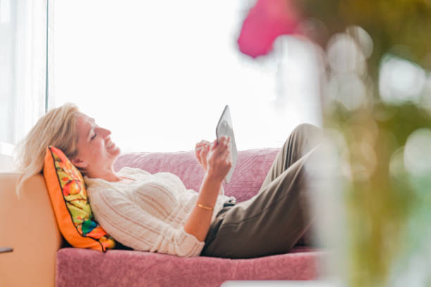 istock Young woman lying on sofa and holding digital tablet 1219984140