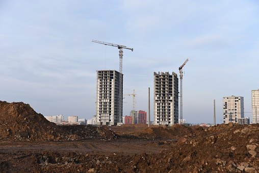 Tower cranes constructing a new residential build. Pouring concrete into formwork of building at construction site. Laying or replacement of underground storm sewer pipes. Concrete drainage pipe.