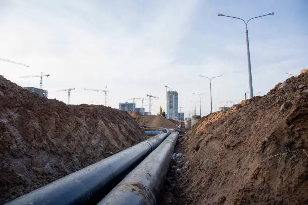 Laying of heating storm sewer pipes at the construction site. Installation of water main and sanitary sewer on background tower cranes and blue sky. Ground water drainage system pipes