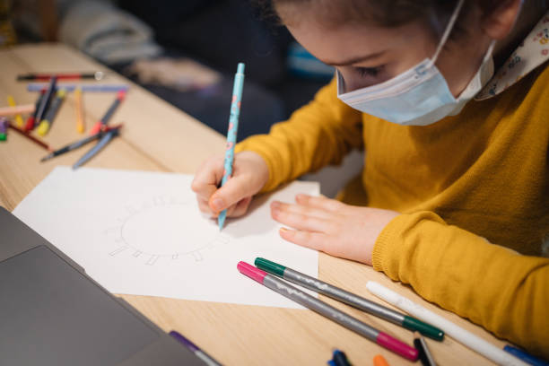 istock A girl in self-isolation with a mask on her face draws a virus 1219990566
