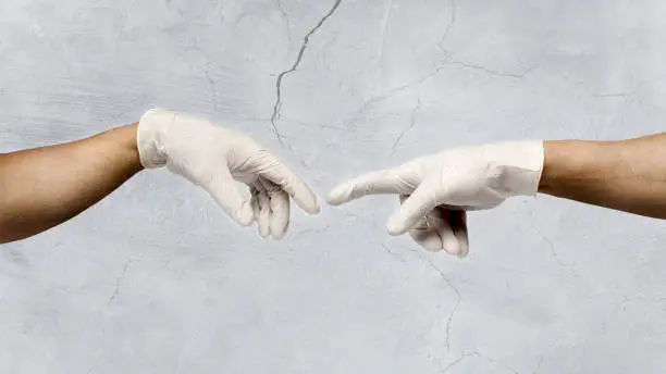 Close-up of two human hands with surgical gloves, reaching out for each other. The creation of Adamo Michelangelo, as symbol of protection against covid-19. The picture has a textured effect to simulate a fresco.
