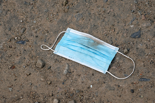 Blue disposable medical mask on the ground. Dirty medical mask lies on the road, environmental pollution. Disposable hygienic mask during a pandemic of the corona virus.