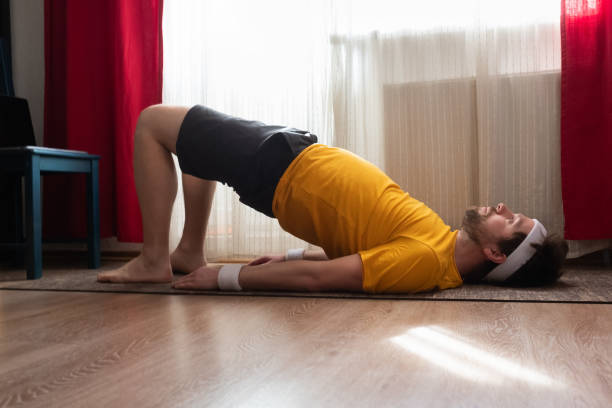 junger mann, der rad pose im wohnzimmer praktiziert yoga - bridge exercise stock-fotos und bilder