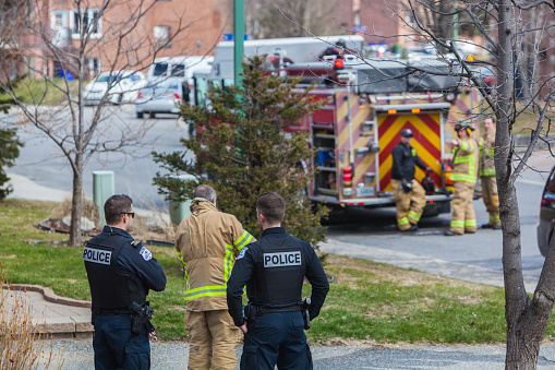 Gatineau, Canada - April 18, 2020: Firefighters and two police officers in action during a residential fire in the time of the coronavirus pandemic.