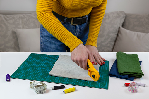 woman in a yellow cuts the fabric. there are quilting tools on the table. patchwork knife, scissors, lined cutting mat, self-locking, thread, centimeter tape. sewing supplies