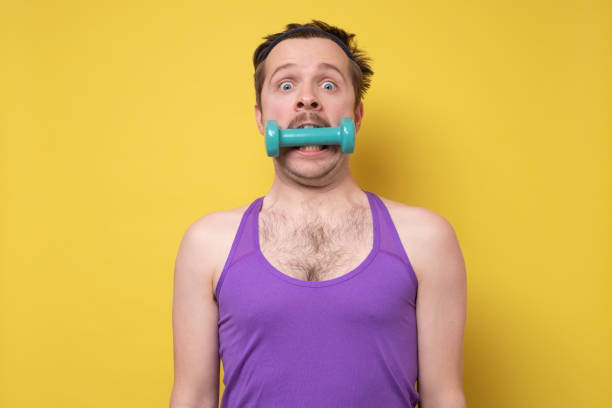 Young sportive man holding a dumbbell in mouth. Funny exercise or healthy teeth concept.