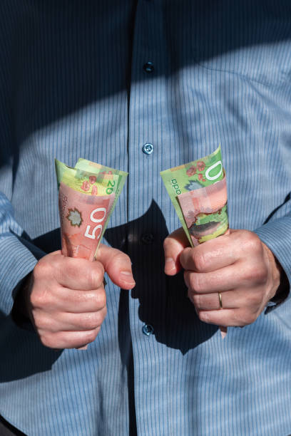 istock Man tightly holding Canadian dollars in both hands in front of chest 1220002870