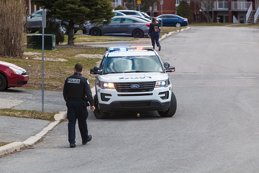 Gatineau, Canada - April 18, 2020: Police car with police officer during the coronavirus pandemic. You can see in the back one woman walking in the street.