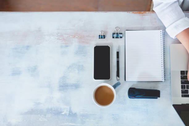 istock Top view of woman using laptop while sitting at the table with laptop, mobile phone, blank note pad and pen. 1220008362