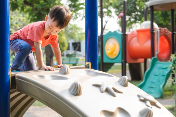 netteasiatische kleinkind kind spaß beim klettern auf künstlichen felsbrocken auf spielplatz, kleiner junge klettern auf eine felswand, hand & auge koordination, motor skills entwicklung - spielgerät stock-fotos und bilder