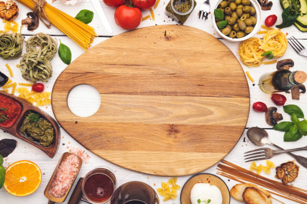 High angle view of an wooden cutting board with food ingredients and spices all around it making a colorful frame on rustic wood table. Useful copy space ready for text