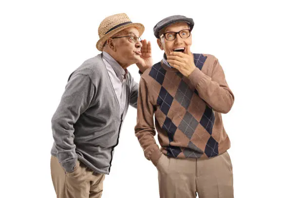 Elderly gentleman whispering a secret to another elderly man isolated on white background