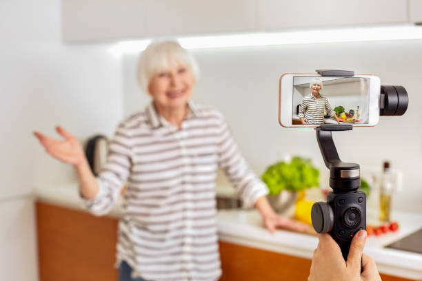 istock Retirement. Senior woman blogger standing at kitchen while being recorded on smartphone for culinary vlog close-up smiling friendly 1220021828