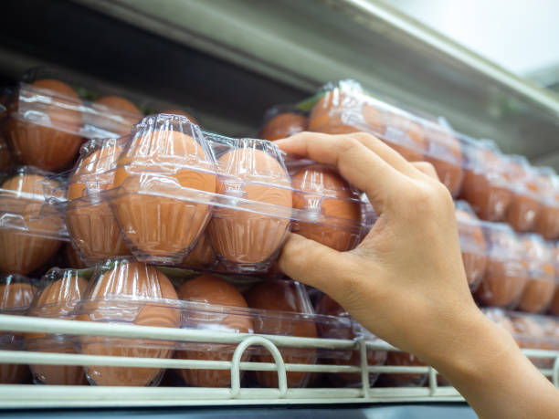 Hand picking raw of eggs in a plastic egg tray from shelf in store.