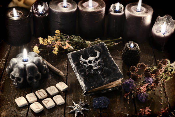 istock Runes, old diabolic book and black burning candles on witch table. 1220046377