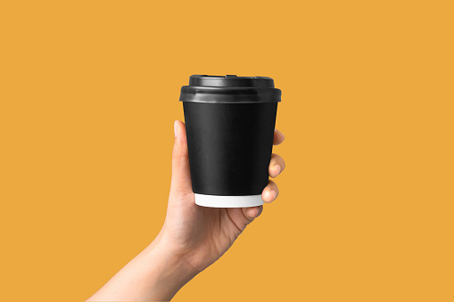 closeup of women hand holding paper coffee cup on yellow background