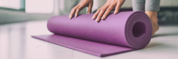 Yoga at home woman rolling pink exercise mat in living room starting warm up meditation zen well being wellness banner panoramic apartment living room lifestyle Yoga at home woman rolling pink exercise mat in living room starting warm up meditation zen well being wellness banner panoramic apartment living room lifestyle. mat stock pictures, royalty-free photos & images