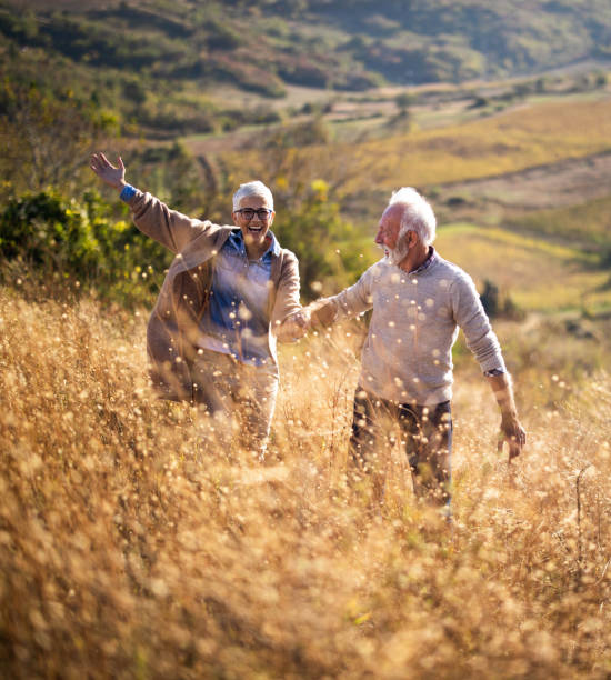 秋の日に丘の上を歩きながら楽しんで幸せなシニアカップル。 - senior adult fun autumn senior couple ストックフォトと画像