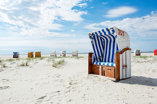 Blue and white striped wooden beach chair or bench on a white sandy tropical beach in hot summer sunshine in a travel and vacation concept