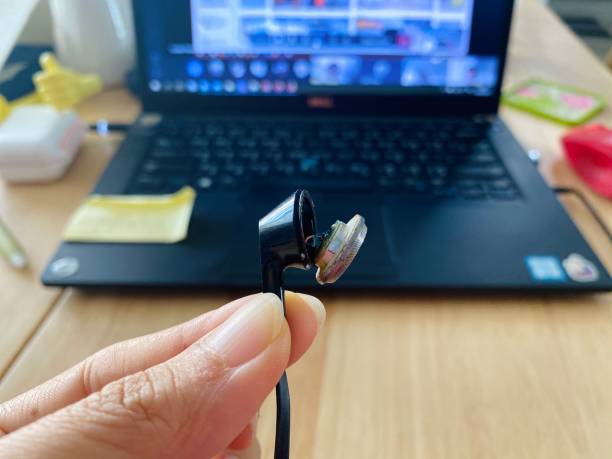 istock Broken Headphone with blurred background of laptop , notebook on wooden table. Working in house. Work from home conference and work hard concept 1220061830