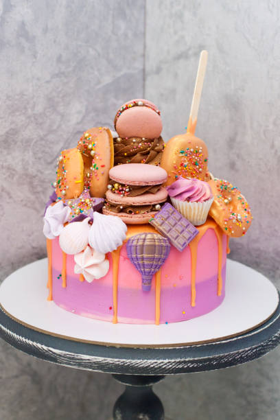 bolo de aniversário rosa e laranja decorado com macaroons, merengues, rosquinhas, cones de waffle, bolos e barras de chocolate. - gateaux cake birthday decorating - fotografias e filmes do acervo