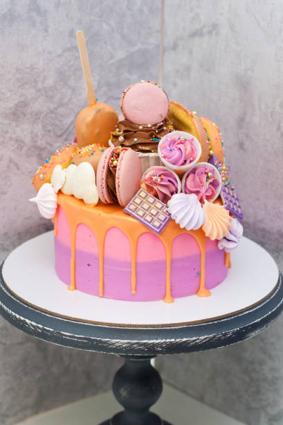 розовый и оранжевый торт ко дню рождения, украшенный макаронами, безе, пончиками, вафельными конусами, тортом и шоколадными батончиками. - cake chocolate cake chocolate gateaux стоковые фото и изображения