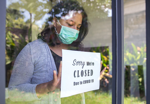 Portrait shot of an Asian restaurant owner putting a closing down poster into a door window due to Covid 19 outbreak